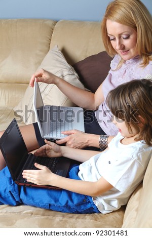 Mother and her young son sit on the sofa and work on small netbook computers