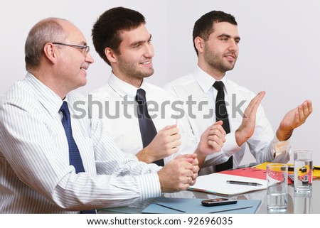 Three businessman, one mature and two young ones sitting at table during meeting