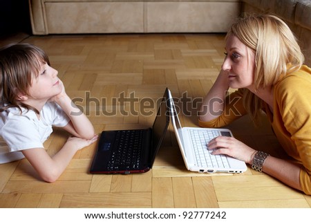 Mother and her 6 year old son working or playing on two small laptops