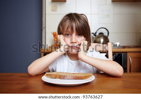 Boy sits at kitchen table and refuse to eat his meal