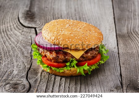 hamburger with grilled meat and cheese on a wooden surface