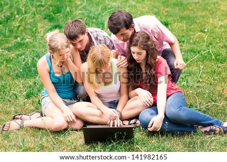 Group of happy smiling Teenage Students Outside College looking excited in laptop sitting on a grass