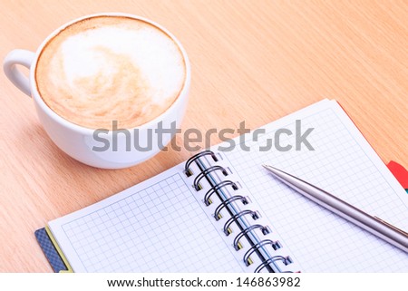 Open blank note book with coffee cup and a pen on wood table