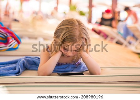 Cute little girl learning with tablet pc on the beach