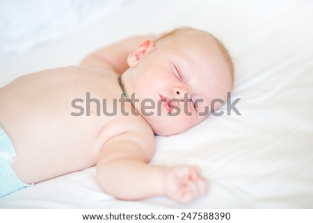 Peaceful newborn baby lying on a bed sleeping on white sheets