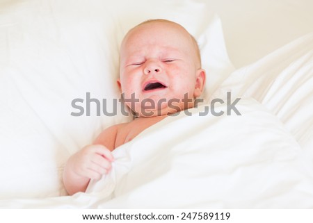 Peaceful newborn baby crying in a bed on white sheets
