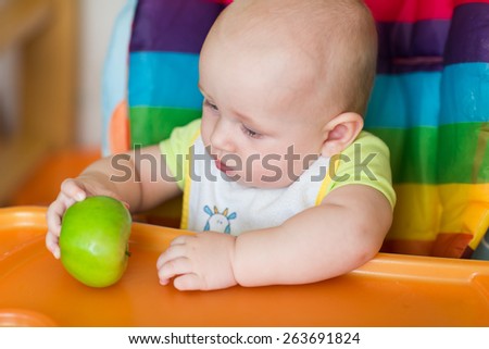 Adorable baby eating apple in high chair. Baby\'s first solid food