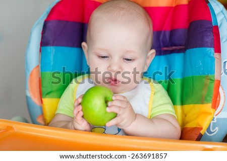 Adorable baby eating apple in high chair. Baby\'s first solid food