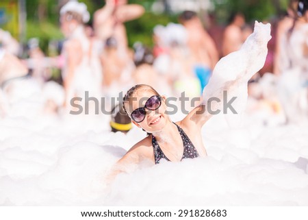 Foam Party on the beach. Cute little girl having fun and dancing.