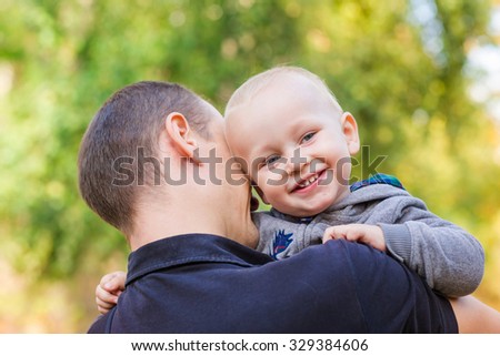 Happy father and his son outdoors. Child hugging daddy and looking out behind his back