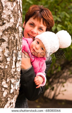 Mother holding baby girl in hands playing peek-a-boo behind the birch