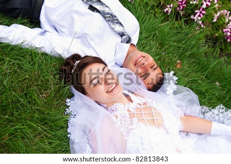 Happy smiling bride and groom  lying on a green grass laughing