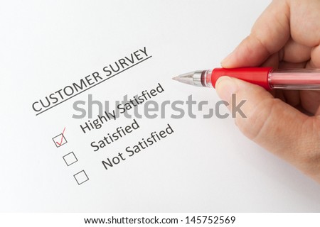 Hand holding a pen and filling a  customer survey with options of highly satisfied, satisfied and not satisfied