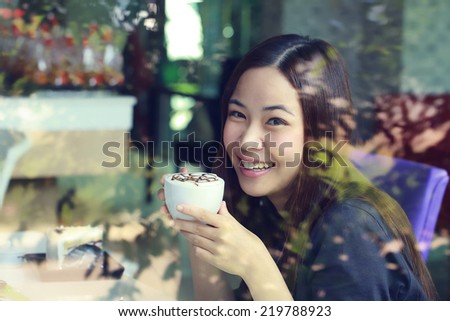 Young Asian women holding a cup of coffee with split tone beside mirror in cafe shop