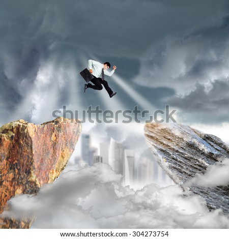 Businessman jump over precipice mountain rock on over blue sky.