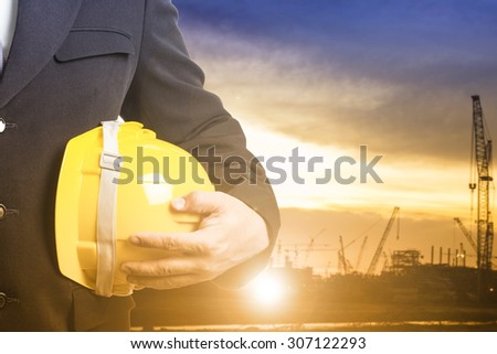 Engineer holding safety hat  beside of construction site progress in twilight time.