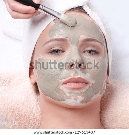 Young beautiful girl receiving clay facial mask in spa beauty salon