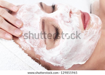 Young beautiful girl receiving white facial mask in spa beauty salon