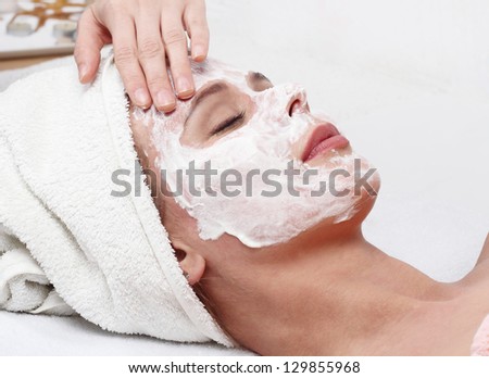 Young beautiful girl receiving white facial mask in spa beauty salon