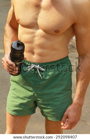 Close up  on Strong muscular man body,  abs, six pack, holding bottle of water. Refresh after summer outdoor workout