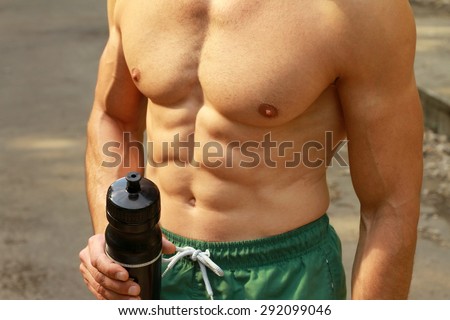 Close up  on Strong muscular man abs , six pack, holding bottle of water. Refresh after summer outdoor workout