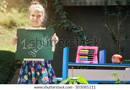 Beautiful girl holding chalkboard with words first grade. Outdoor portrait