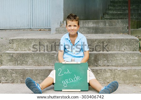 Boy holding Chalkboard with words Second Grade. Outdoor photo