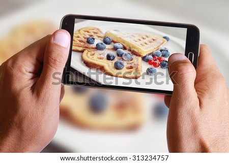Male hand taking photo of waffles with blueberries with cell, mobile phone.
