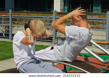 Father and son during street workout in outdoor gym. Strong man and little boy. Family, sport, fitness, active lifestyle concept