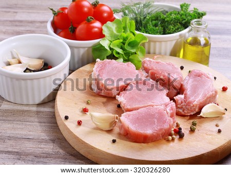 Fresh raw pork fillet medallions with salad, olive oil and cherry tomatoes on wooden cutting board. Healthy lifestyle