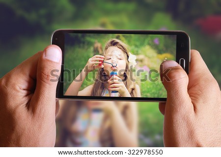 Male hand taking photo of Vintage Portrait of beautiful girl blowing bubbles with cell, mobile phone. Kids, childhood, family concept.