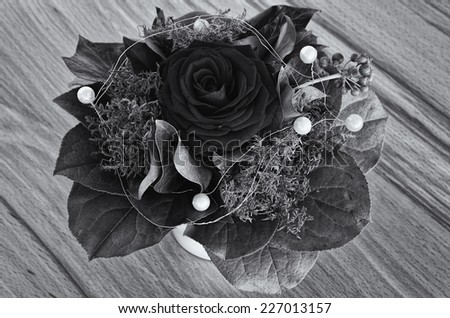 Black Rose, Black and White - Single red rose with greenery and deco beads in a bouquet, in a vase, on a wooden ground, in black and white.