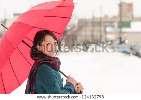 Young Asian woman holding up her umbrella in winter city