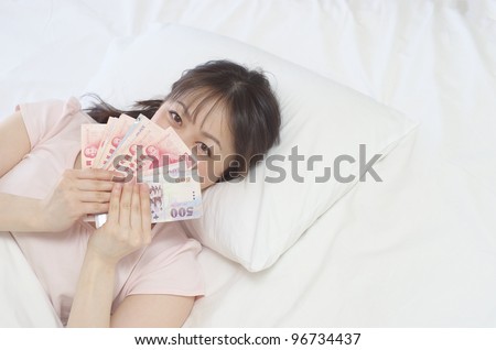 Young Asian woman holding New Taiwan Dollars on the bed