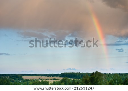 Bright rainbow in the sky with clouds above the forest on sunset