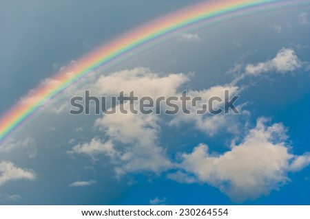 Bright rainbow in the blue sky with white clouds