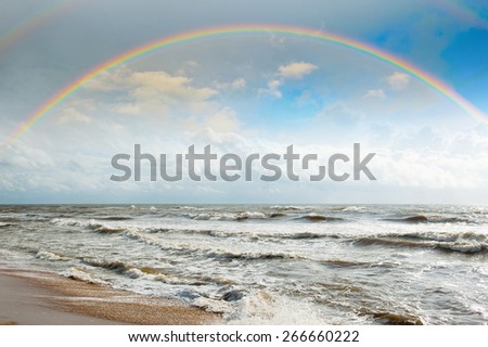Bright rainbow in the sky with clouds above the ocean