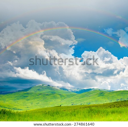 Bright double rainbow in the sky with clouds above the mountains in summer day