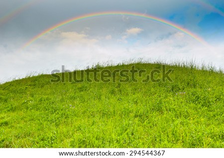 Bright rainbow in the sky with clouds above the hill