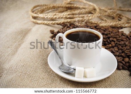 Cup of coffee with coffee beans on the table covered with a sackcloth