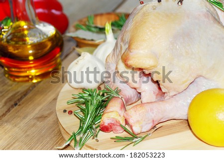 Raw whole chicken on the board with lemons ans rosemary