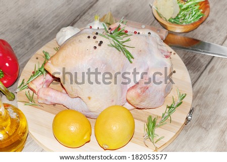 Raw whole chicken on the board with lemons ans rosemary