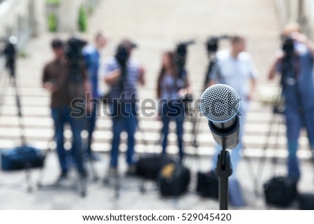 Microphone in focus against blurred camera operators and journalists. Press conference.