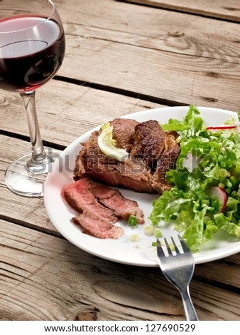 Veal meat with green salad with a red wine glass