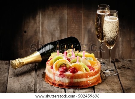 Jellied fruits cake with six birthday candles and champagne on wood