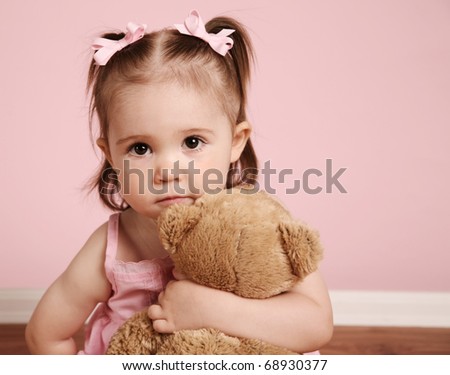 Portrait of an adorable toddler girl hugging a teddy bear on a vintage pink background