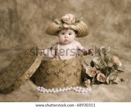 Portrait of an adorable baby girl playing dress up, sitting in a hatbox wearing a straw hat and pearl necklace