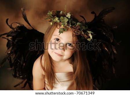 Portrait of a beautiful young girl dressed up as an angel with brown wings and a gold dress, wearing an ivy crown
