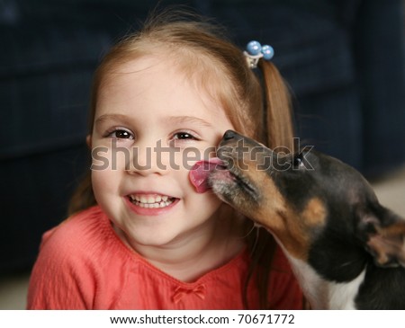 Portrait of a beautiful smiling young girl being licked on the cheek by a cute terrier puppy dog