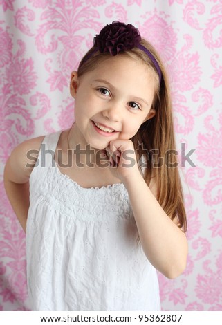 Portrait of a beautiful young girl wearing a purple flower hair bow with pink damask background in studio